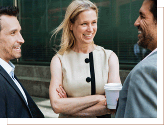 A woman and two men laughing while talking over coffee in a business setting.