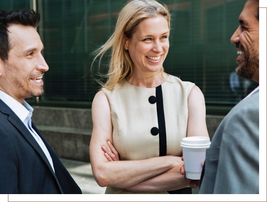 A woman and two men laughing while talking over coffee in a business setting.