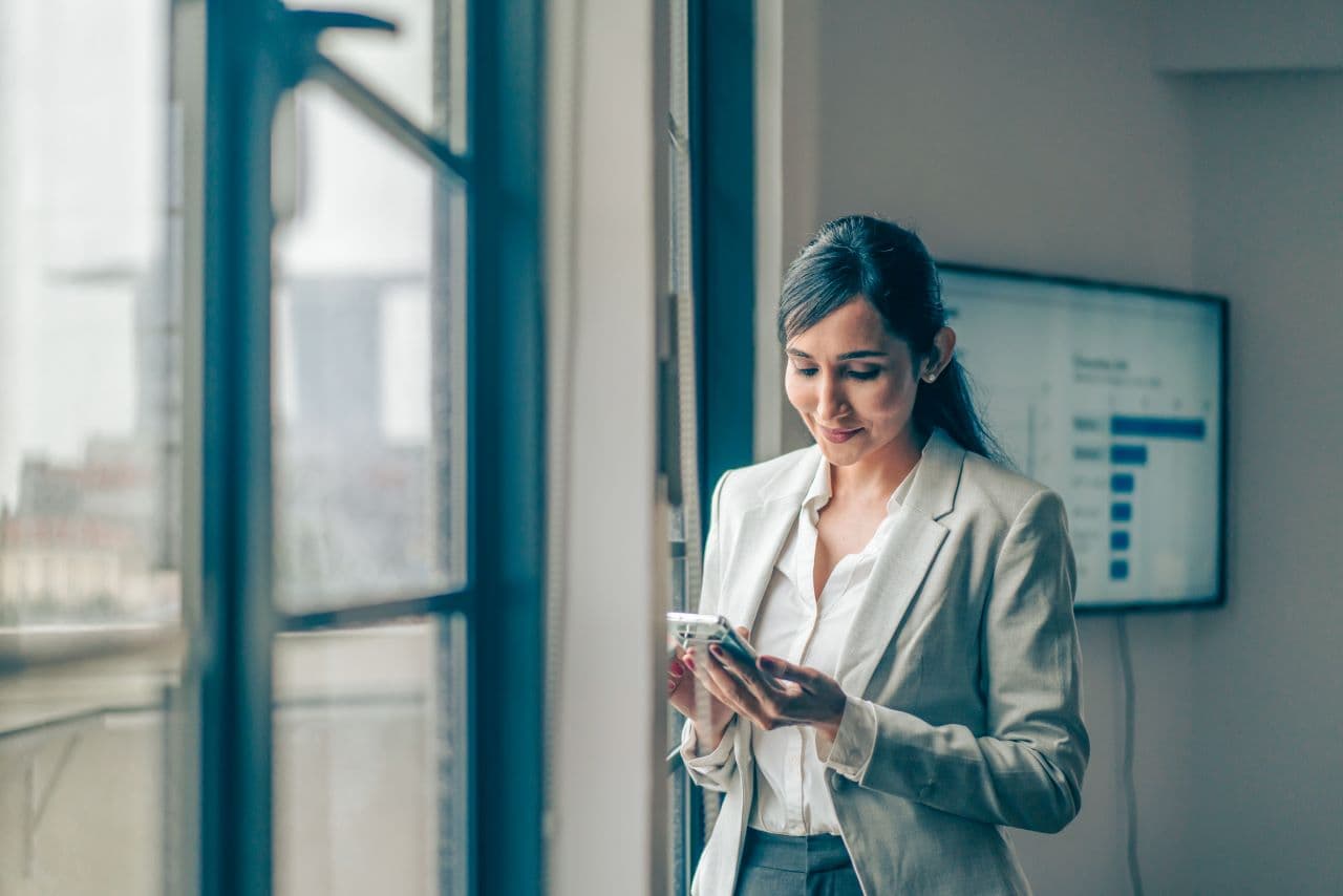 A woman looks down, reading an electronic device in her hands.