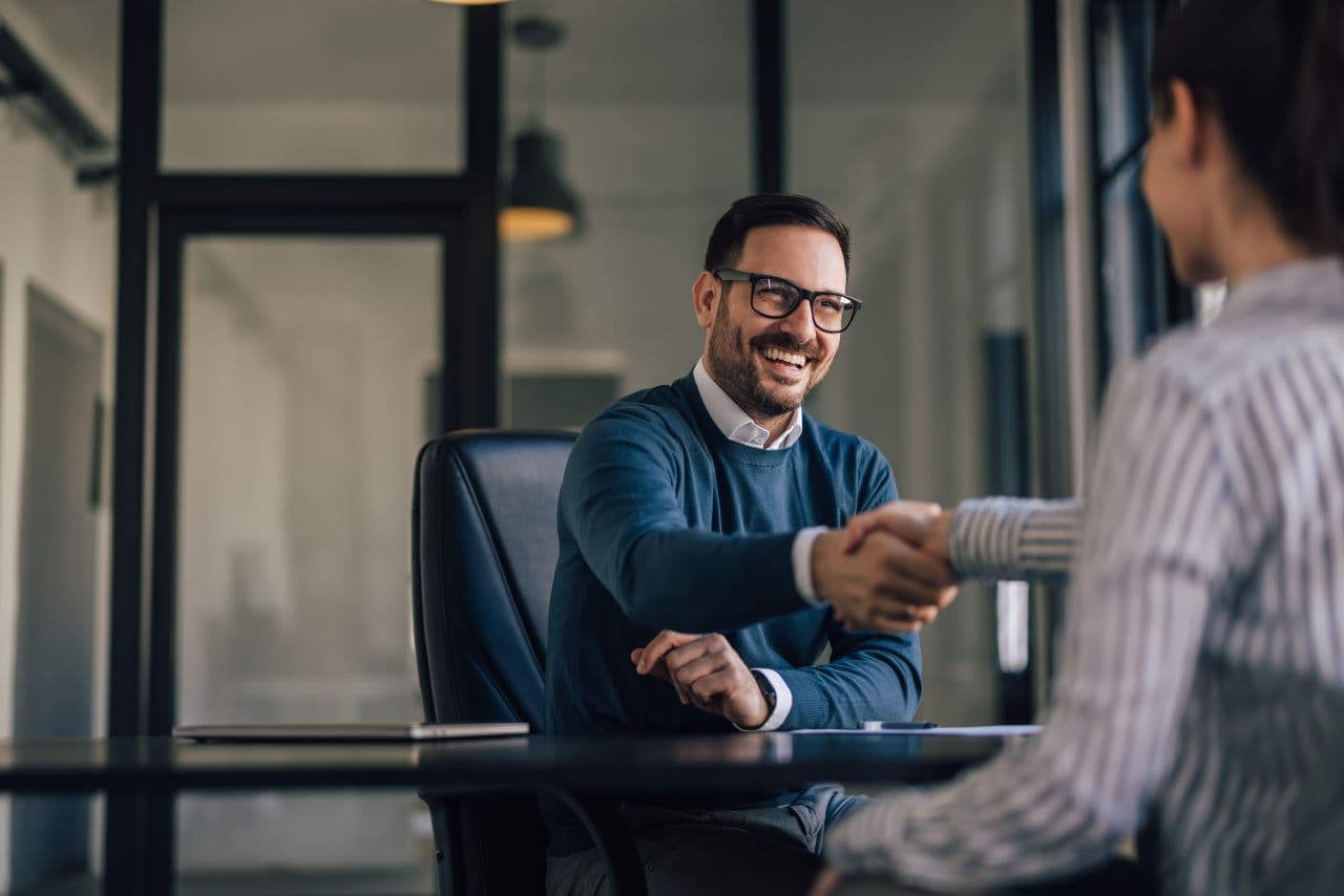 Man smiling while shaking hands with another person across a table.